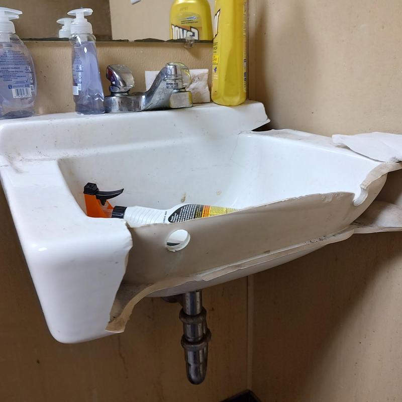 Broken wall hung sink with faucet and cleaning supplies Broken wall hung sink with faucet and cleaning supplies