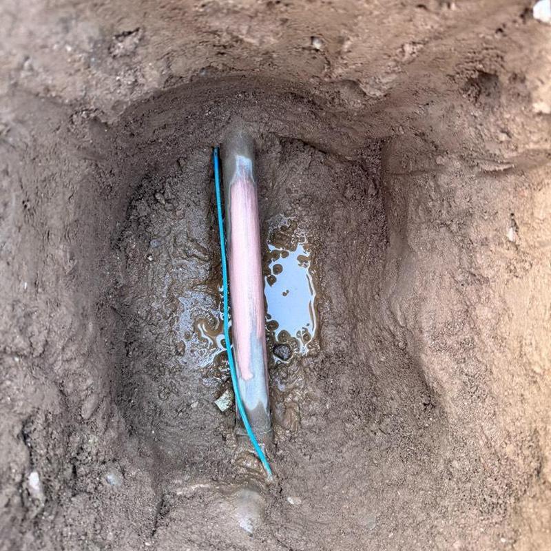 Copper water main exposed in dirt hole with moisture