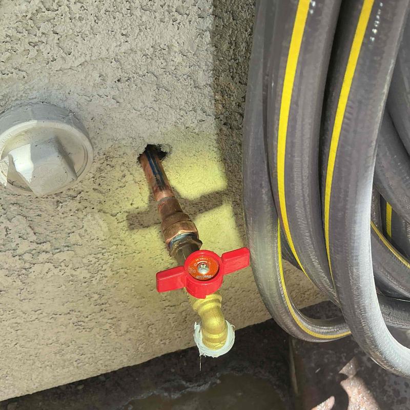 Hose bib with red valve and attached garden hose