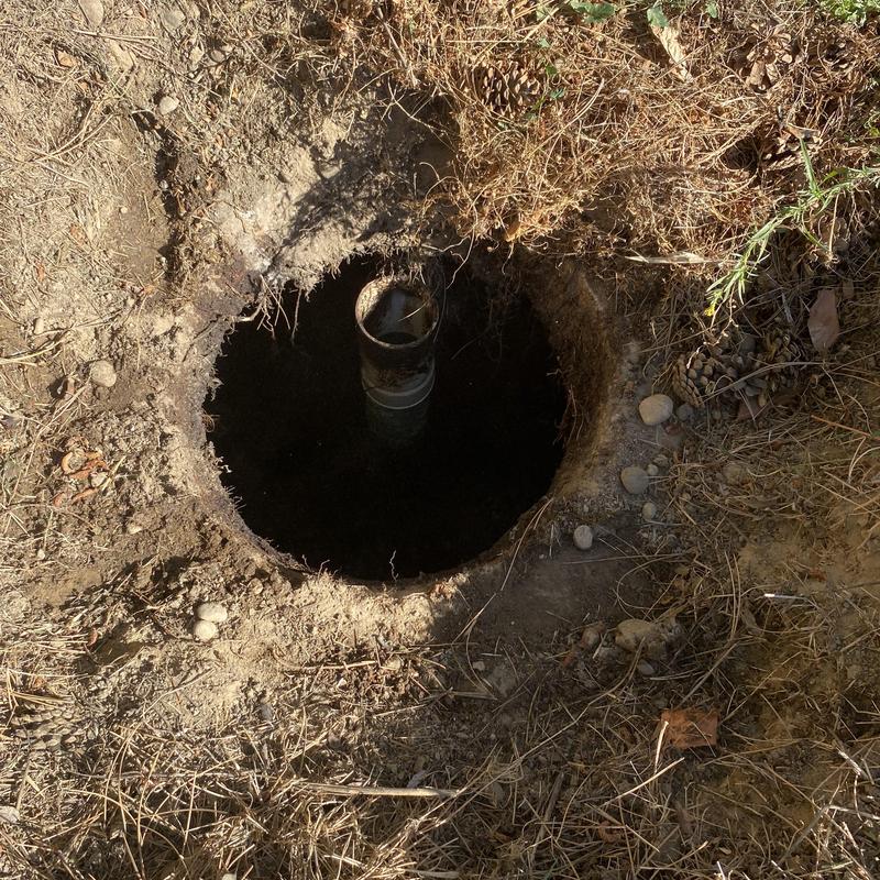 Septic tank lid opening with exposed pipe in dirt