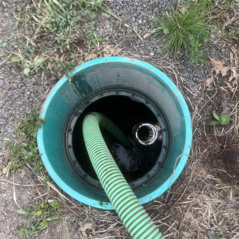 Septic tank lid open with green pump-out hose inserted