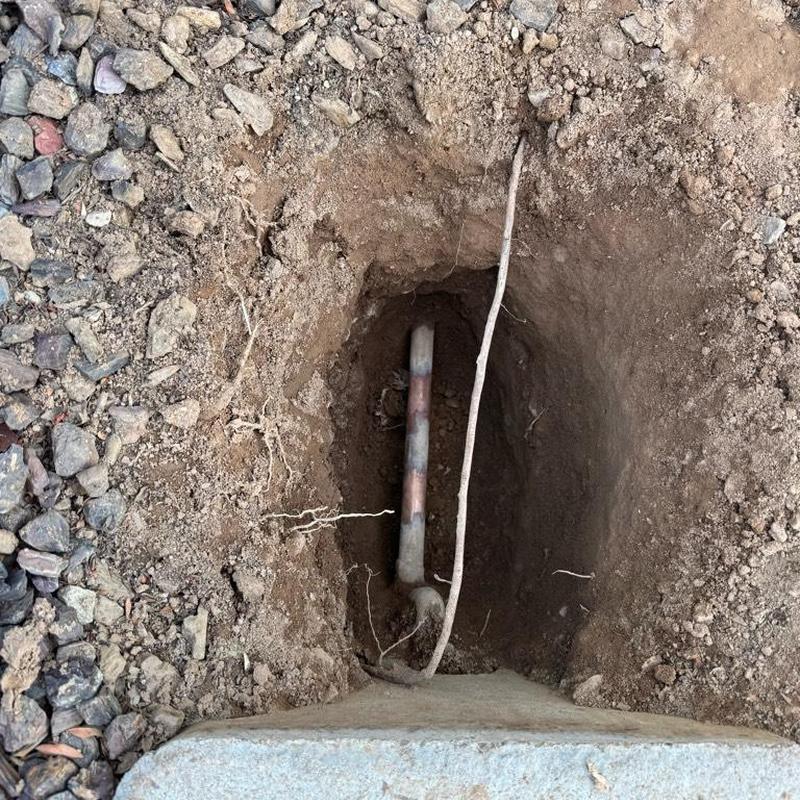 Copper water main pipe exposed in dirt trench