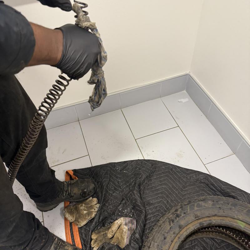 Drain snake clog removal with gloved hands in corner Drain snake clog removal with gloved hands in corner