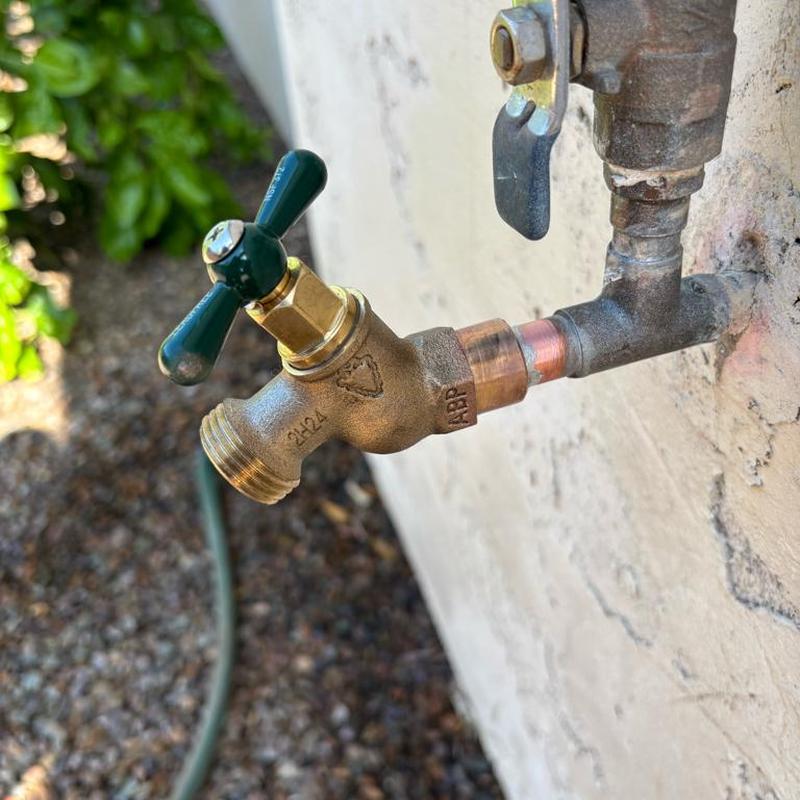 Exterior hose bib with green handle on wall