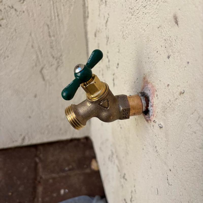 Exterior hose bib with green handle on wall in Queen Creek