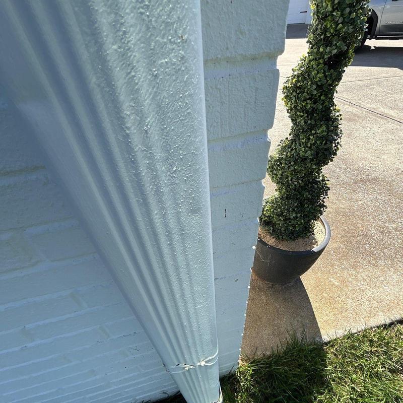 Downspout with minor damage near brick wall and planter