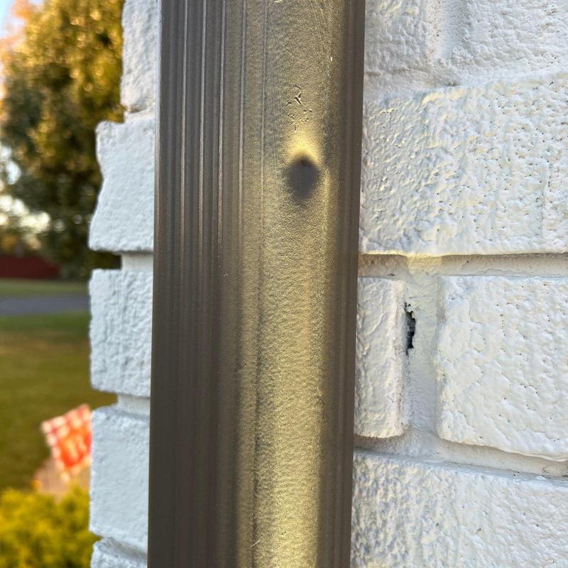 Metal downspout with dent damage on white brick wall