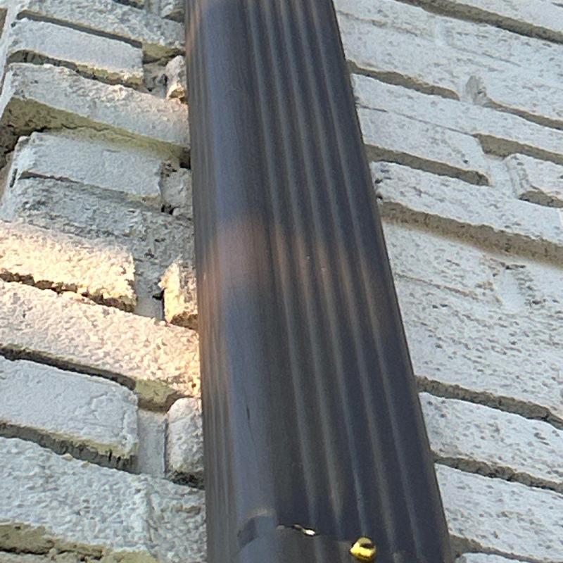 Downspout with dent damage on brick wall exterior