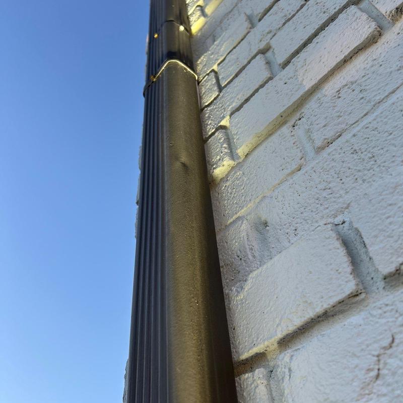 Metal downspout dented on white brick wall