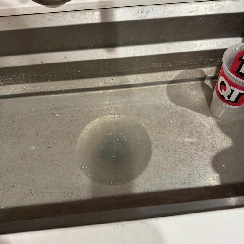 Kitchen sink drain with standing water and cup nearby