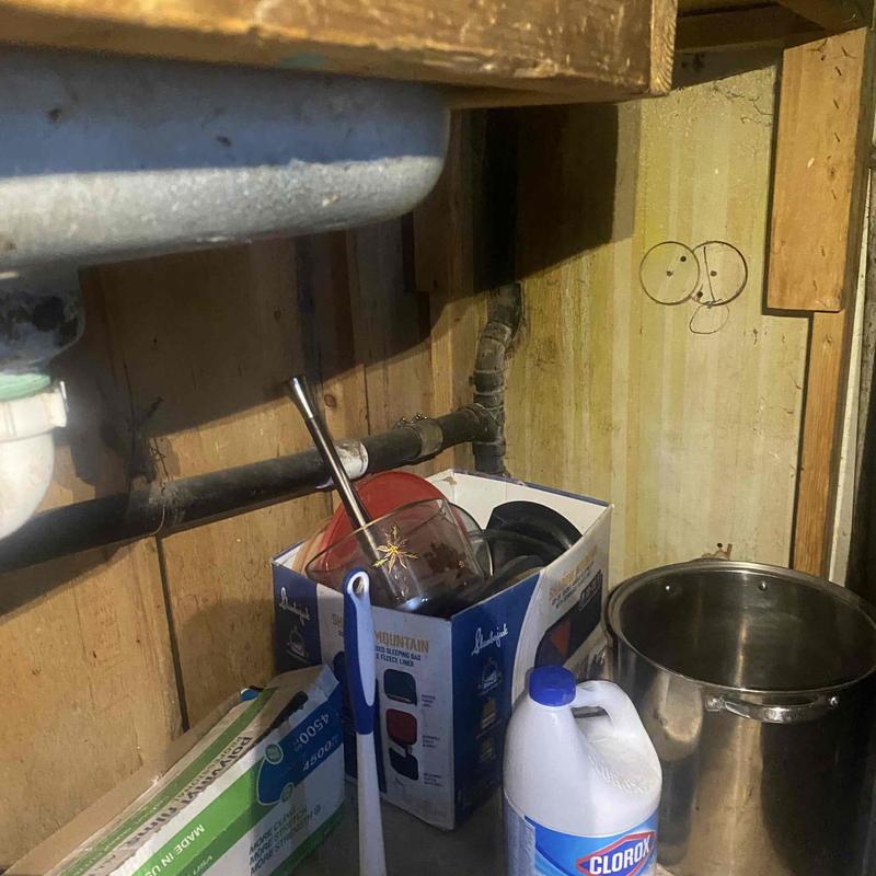 Kitchen sink drain pipes under cabinet with cleaning supplies