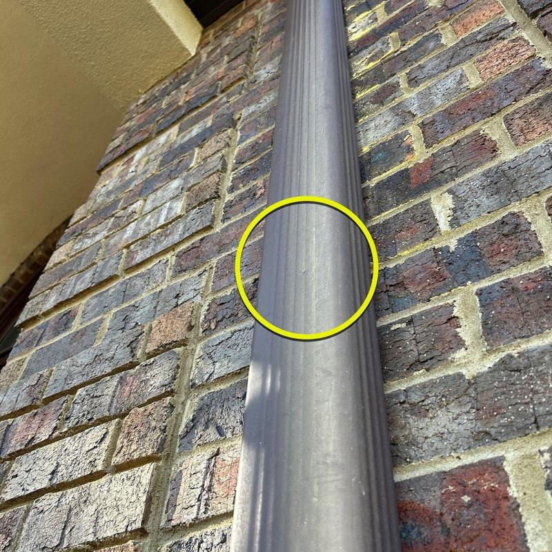 Downspout with dent damage on brick wall close-up