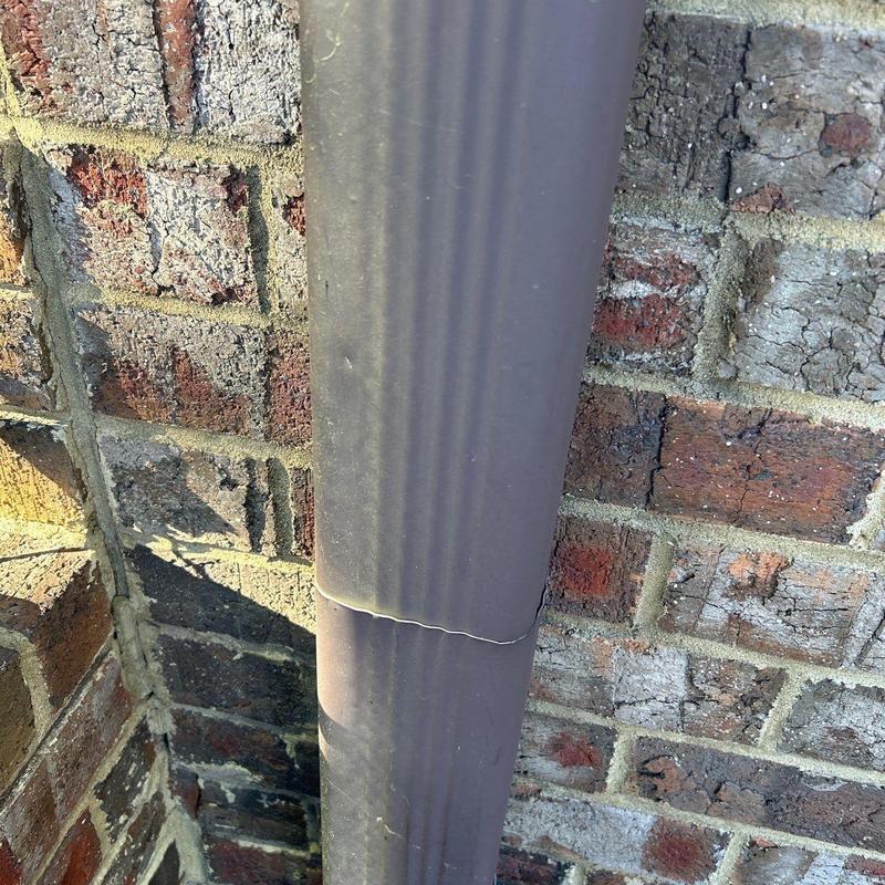 Downspout with visible crack near brick wall