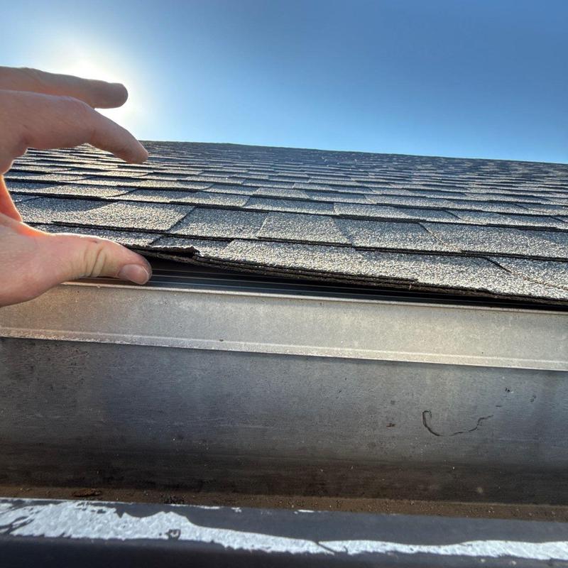 Asphalt shingles lifted above gutter edge by hand