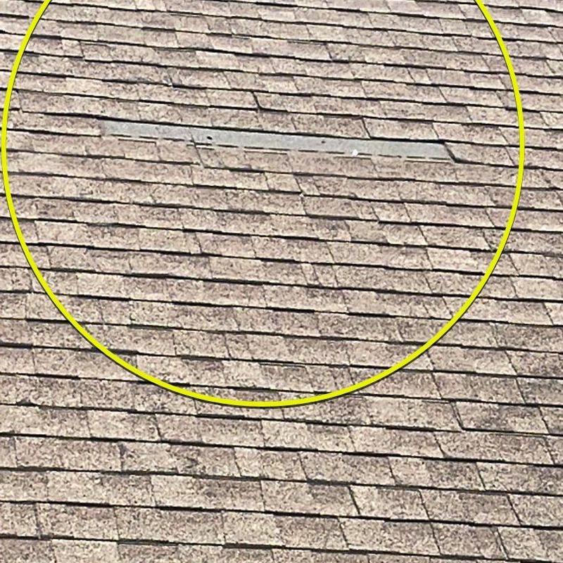 Asphalt roof shingles with wind damage marked by circle