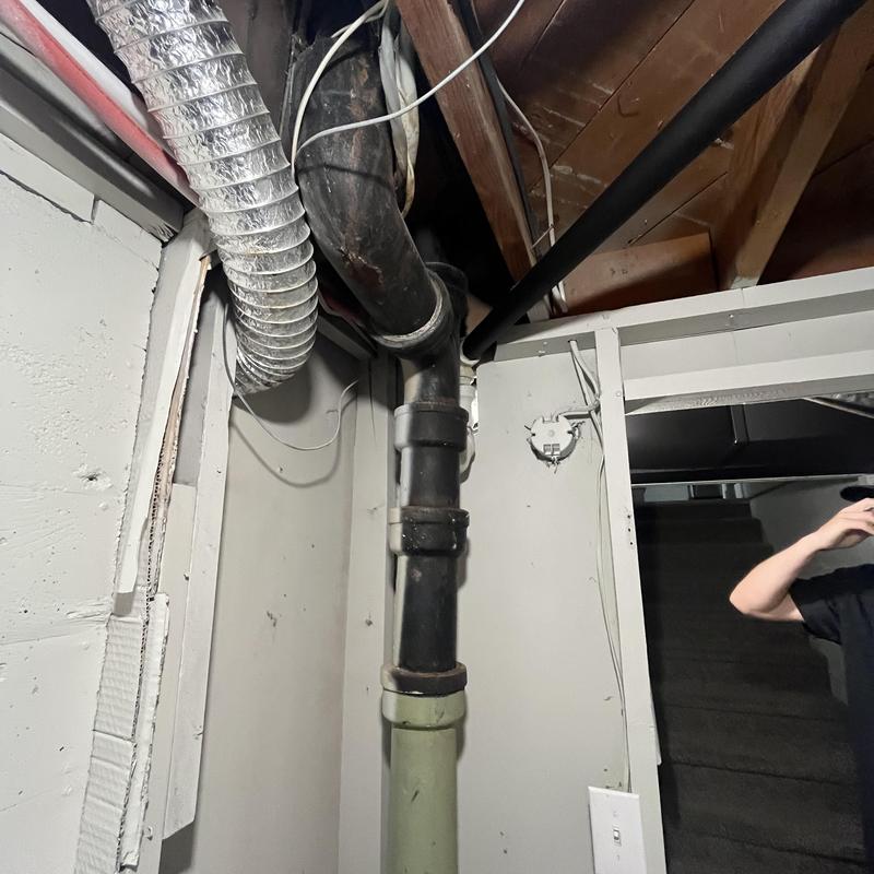 Cast iron waste stack pipe in basement near stairs