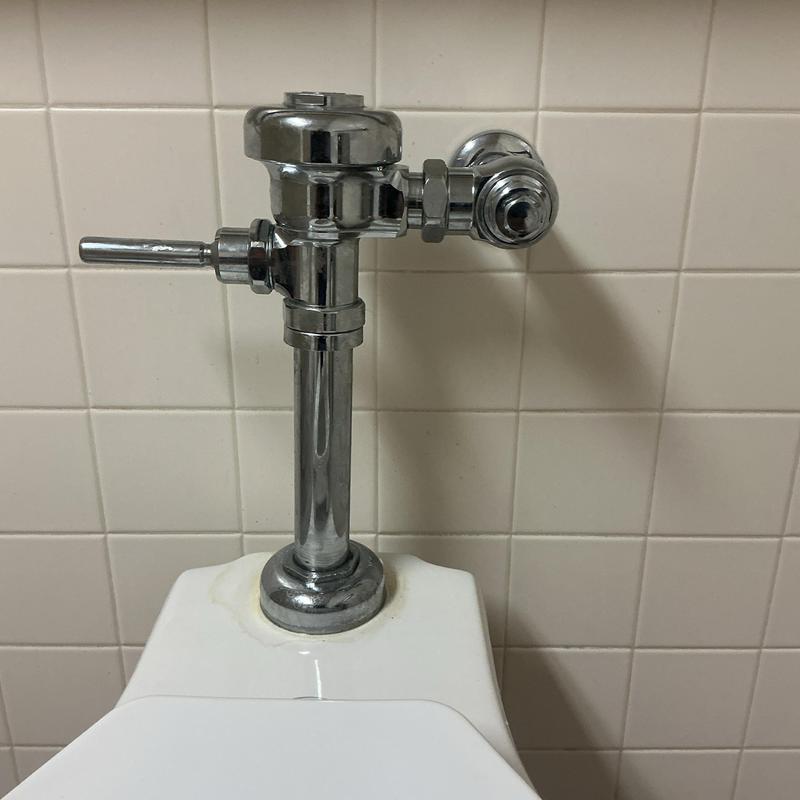 Flushometer valve on commercial toilet with tiled wall Flushometer valve on commercial toilet with tiled wall