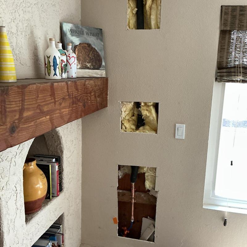 Copper plumbing pipes behind drywall with insulation.