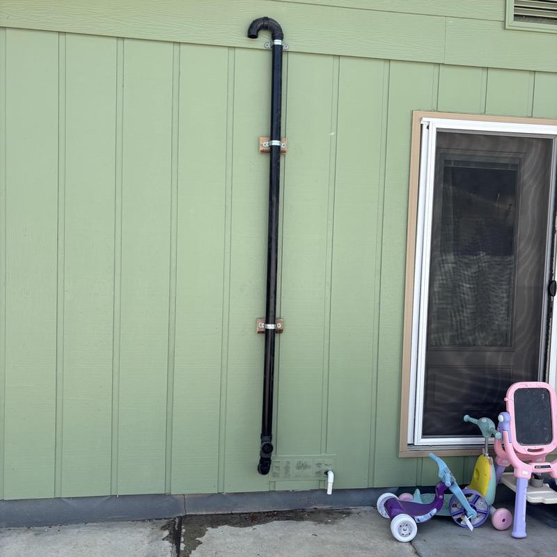 Outdoor drain pipe installation on green siding wall