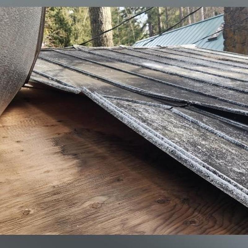 Metal roof panels lifted by wind damage on wooden deck