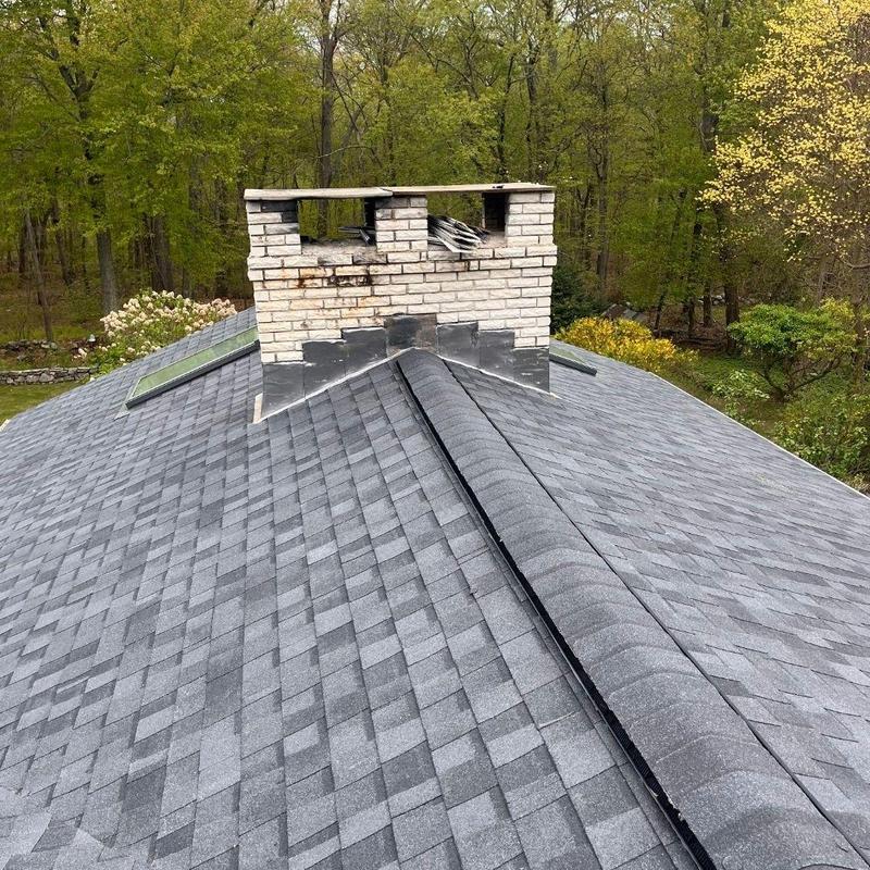 Asphalt shingle roof with brick chimney in wooded area Asphalt shingle roof with brick chimney in wooded area
