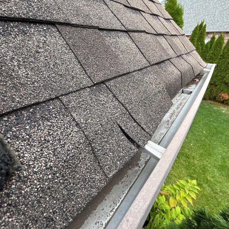 Asphalt roof shingles with visible damage near gutter