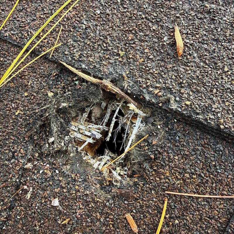 Damaged asphalt shingle roof with hole and debris