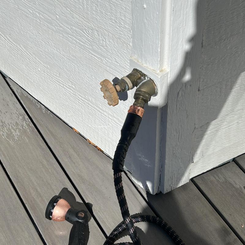 Hose bib with attached garden hose and nozzle outdoors