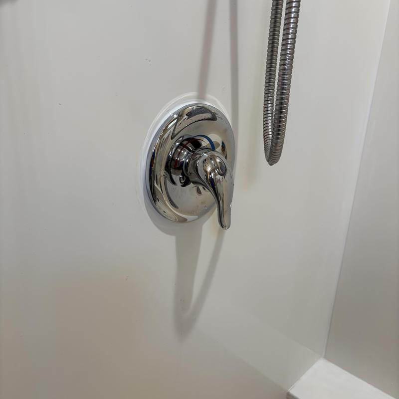 Shower valve handle and metal hose in white tub
