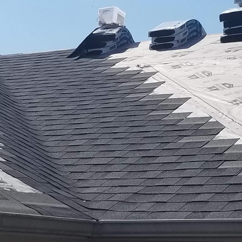 Asphalt shingle roof installation in progress with chimney cap