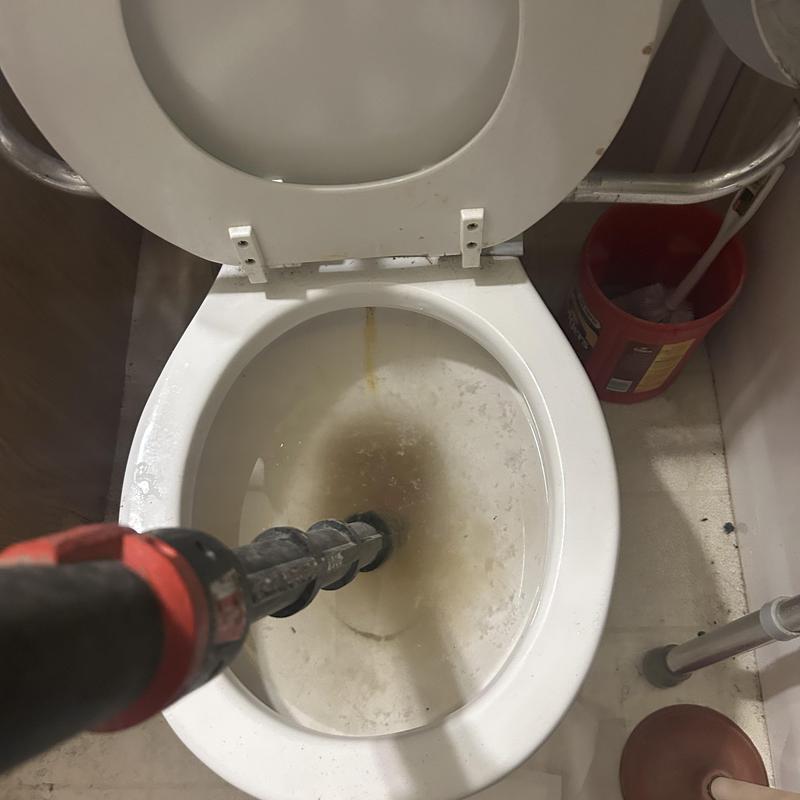 Toilet auger clearing clogged drain in bathroom toilet bowl