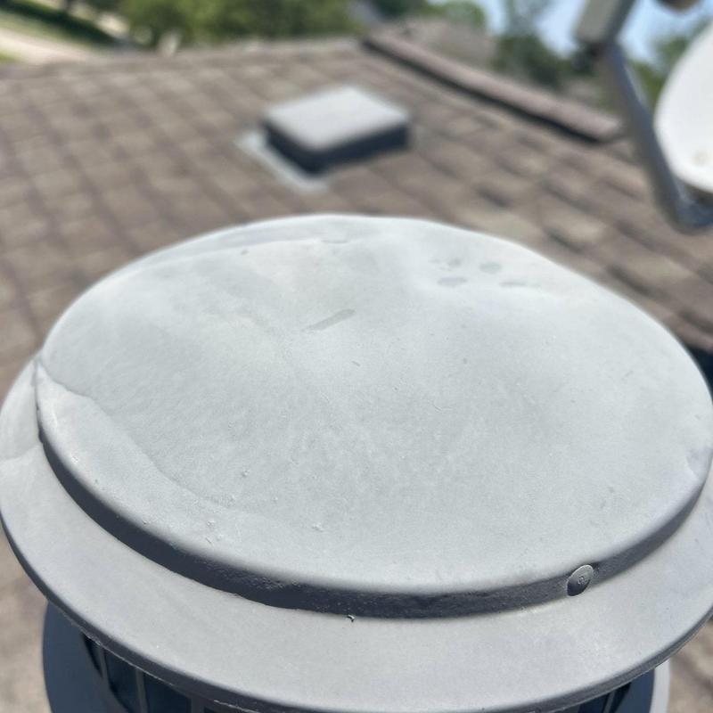 Roof vent cap with hail damage dents on shingle roof