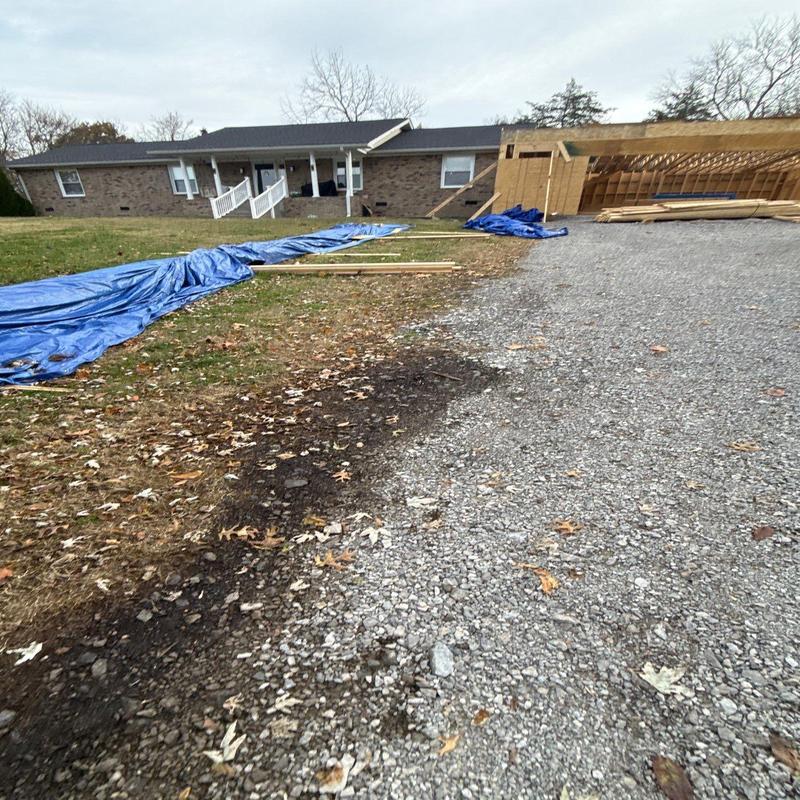 Gravel driveway with leaf debris and tarp-covered lumber