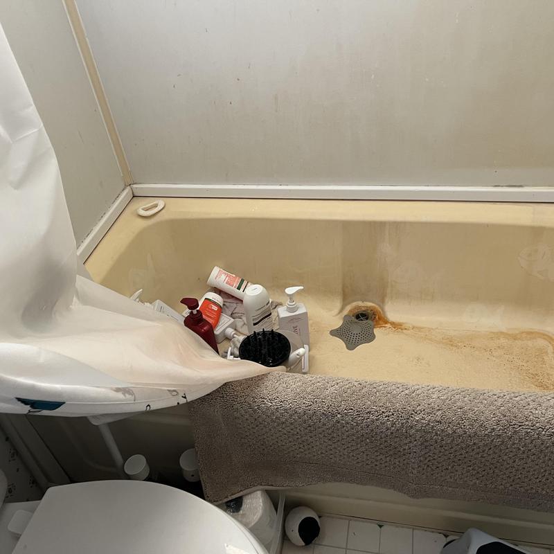 Bathtub with rusty drain and shower curtain pulled back