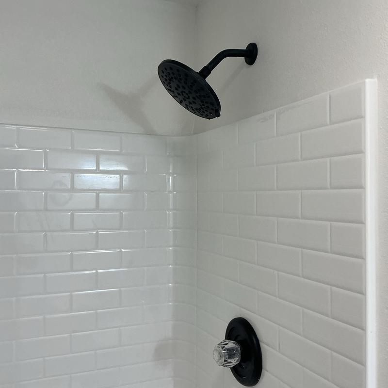 Shower head and valve installed on white tiled wall