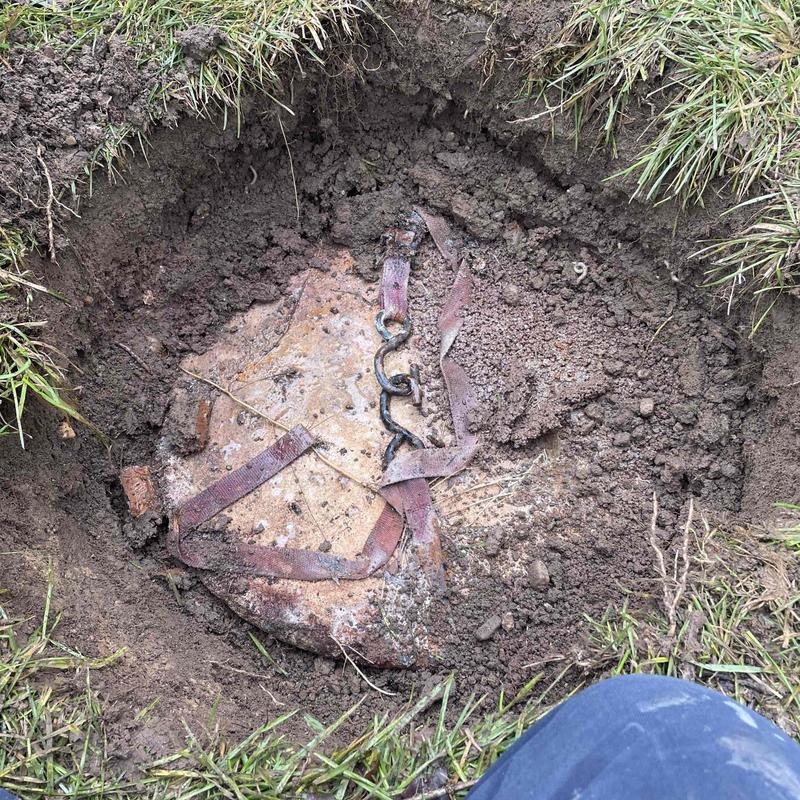 Septic tank lid exposed in dug hole outdoors