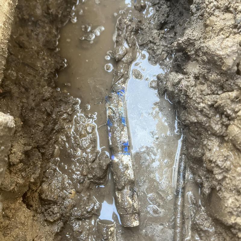 1-inch irrigation main with exposed leak in muddy trench