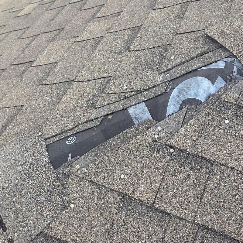 Asphalt roof shingles with hail damage and exposed underlayment
