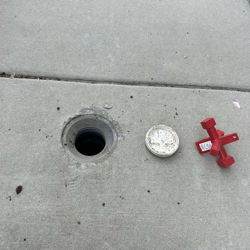 Commercial mainline access point with removed lid and tool on concrete