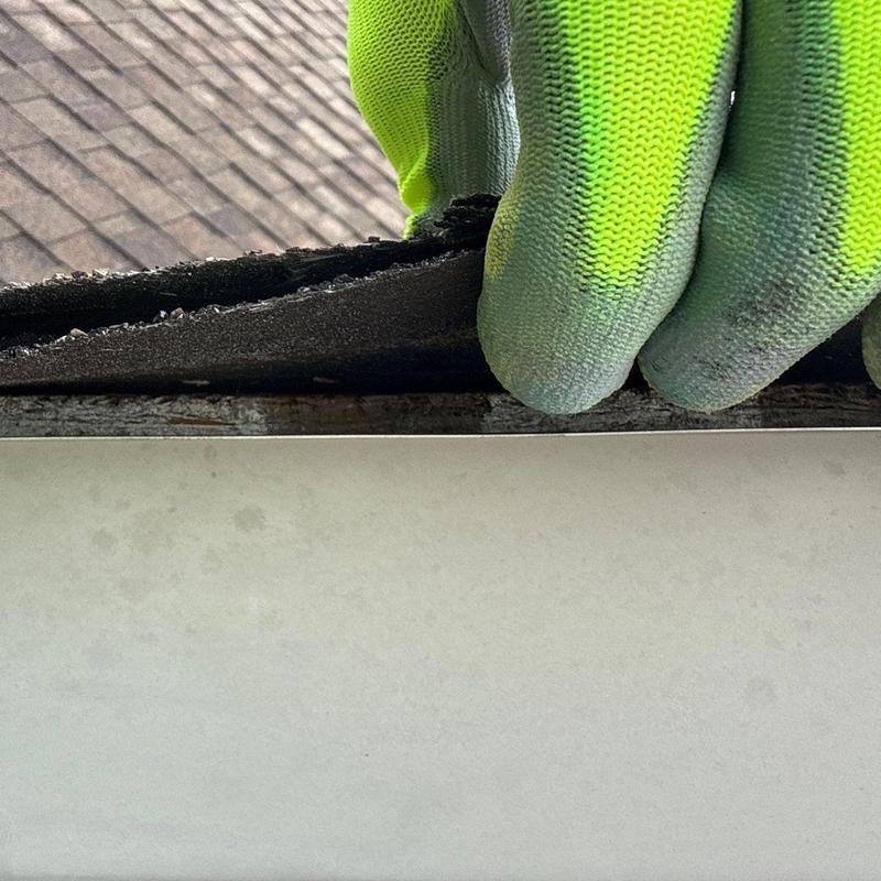 Asphalt shingle edge lifted by gloved hand on roof edge