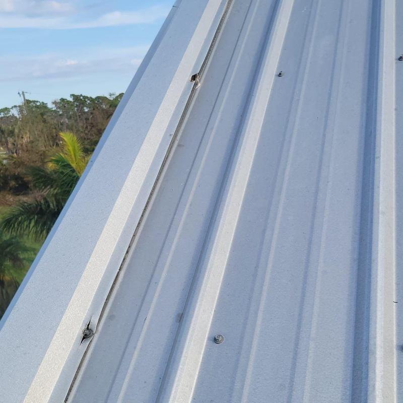 Metal roof panel with wind damage and loosened screws