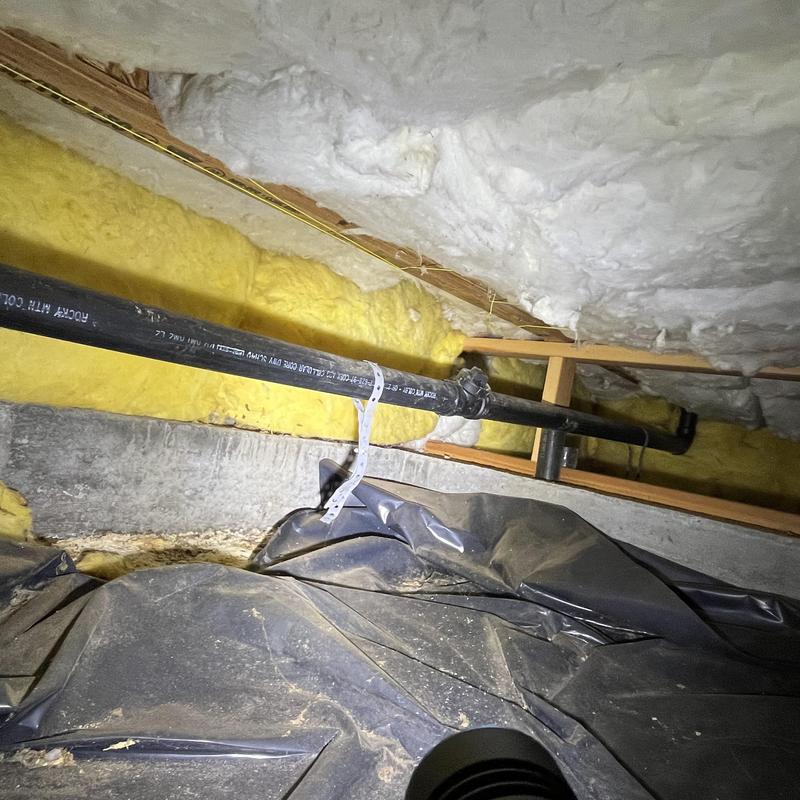 Black PVC plumbing pipe installation in insulated crawlspace