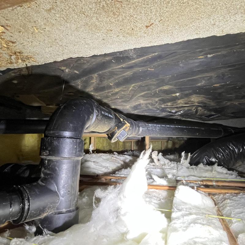 Black PVC plumbing pipes in crawl space with insulation