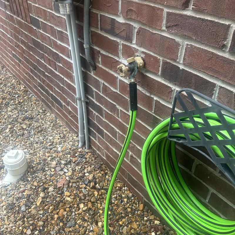 Outdoor hose bib valve with green garden hose attached