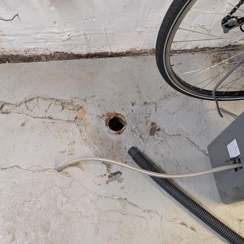 Concrete floor drain hole with nearby cables and bike tire Concrete floor drain hole with nearby cables and bike tire