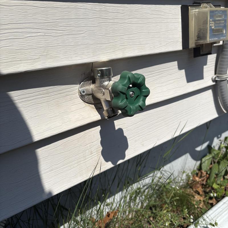 Frost-free outside faucet with green handle on siding