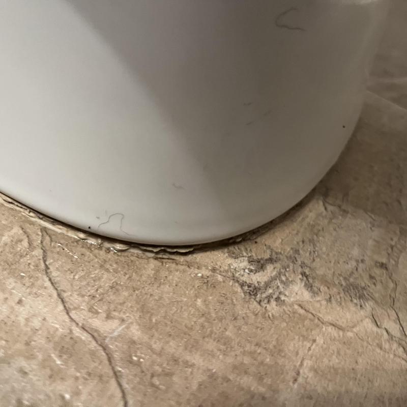 Toilet base with worn wax ring seal on tile floor