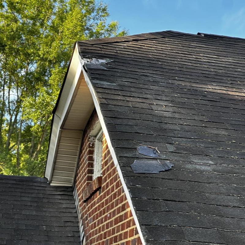 Roof shingles with storm damage near house peak Roof shingles with storm damage near house peak