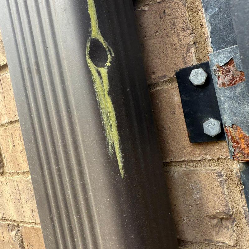 Metal downspout dent with rusted bracket on brick wall