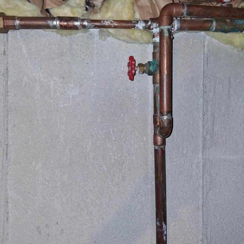 Copper water meter valves with red handle in basement wall